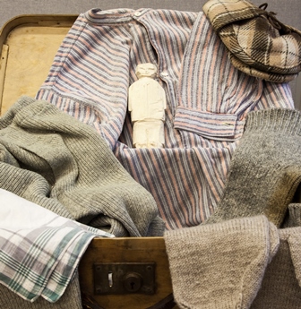 Hellahuoneen Paavo -laukussa on pieni pieni kipsinen ihmishahmo vaatteiden keskellä.