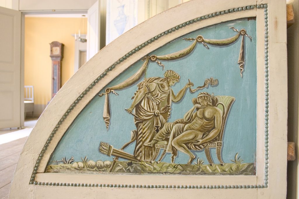 Yksityiskohtakuva Jugend-tyylisen salin sohvanpäädystä. Antiikki aiheinen koristekuva.