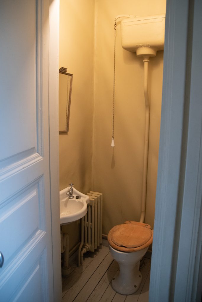 Pieni käsienpesuallas, vessanpönttö ja huuhtelusäiliö, josta roikkuu vetokahva.