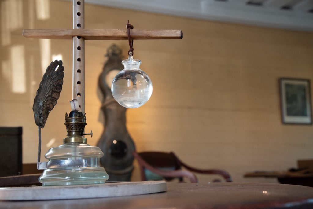 Suutarin pöydällä oleva suutarinlamppu. Vedellä täytetty lasipallo roikkuu puisesta telineestä.